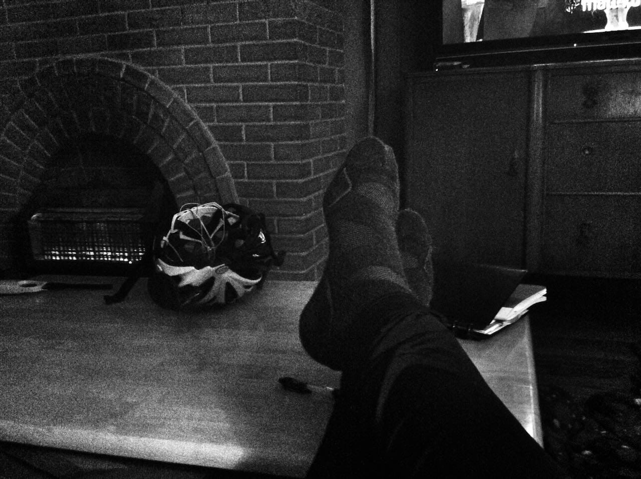 B&W photo of my feet up on a coffee table next to my bicycle helmet.