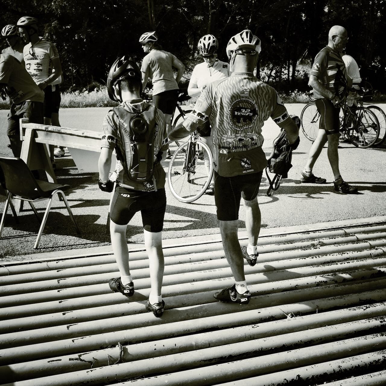 B&W photo of cyclists carefully crossing a cattle guard in bike shoes.