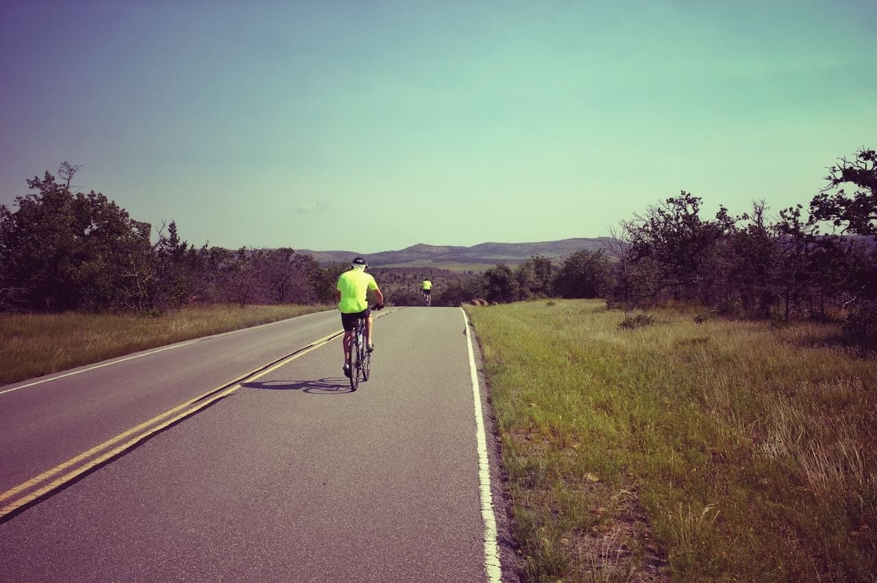 Color photo of a couple of cyclists headed down a paved highway.