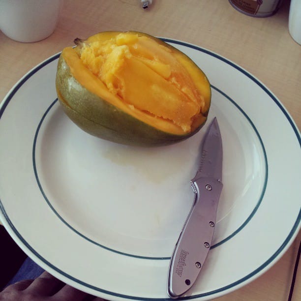 Color photo of opened mango next to a knife.