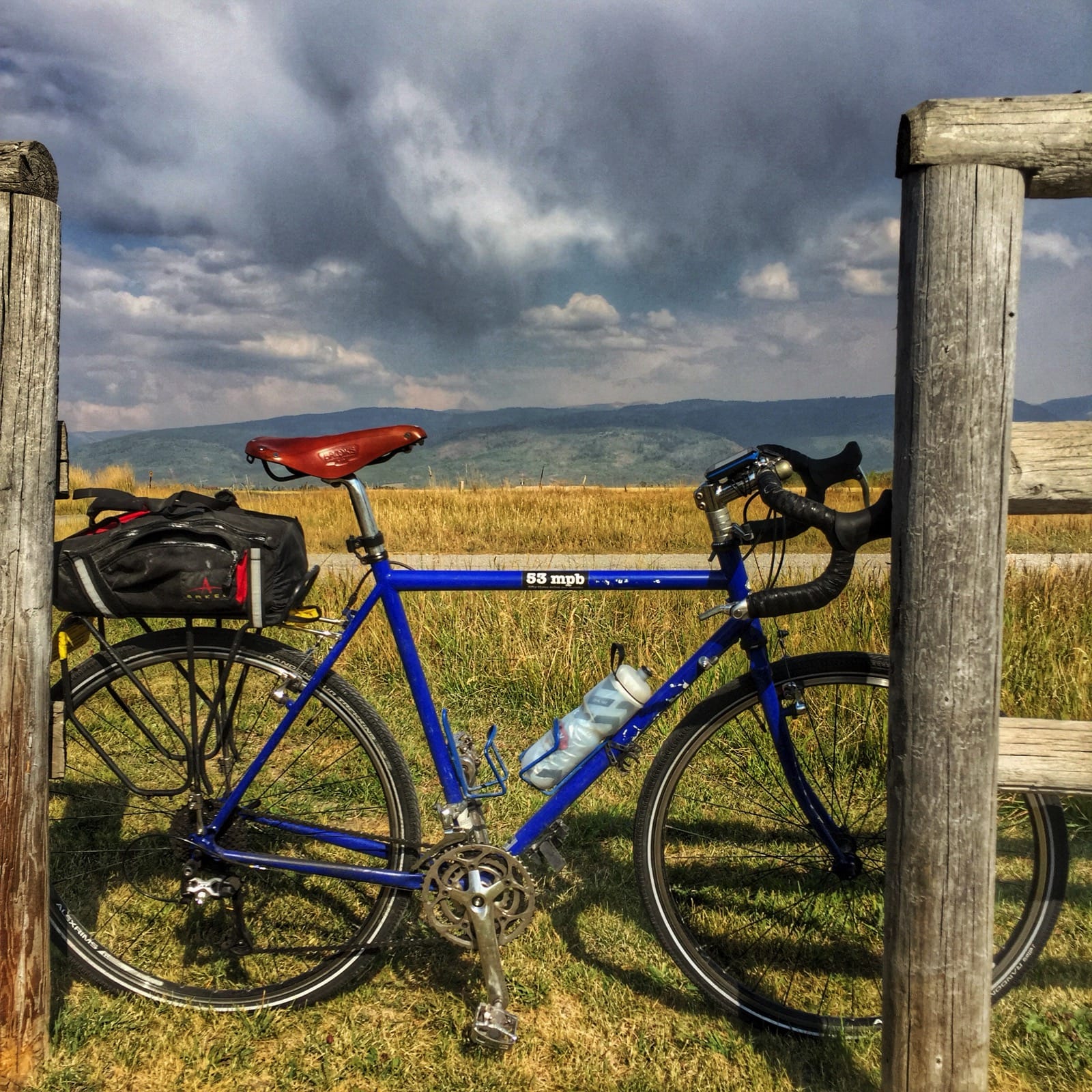 Color photo of a bicycle leaning against a wood fence in the countryside.